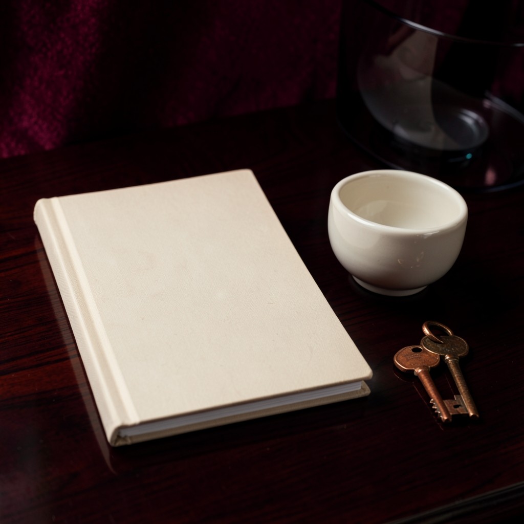 Two closed cloth-bound notebooks, a ceramic bowl, and a copper key on dark wood.